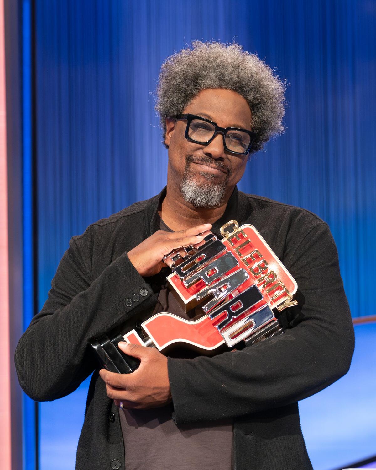 W. Kamau Bell holding his Celebrity Jeopardy! trophy. 